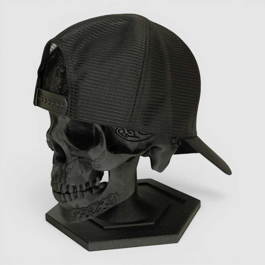 Night Heron Israel black mesh trucker cap displayed on a decorative black skull head stand