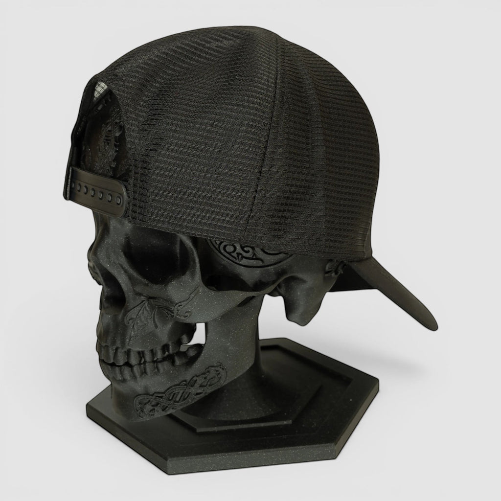 Night Heron Israel black mesh trucker cap displayed on a decorative black skull head stand