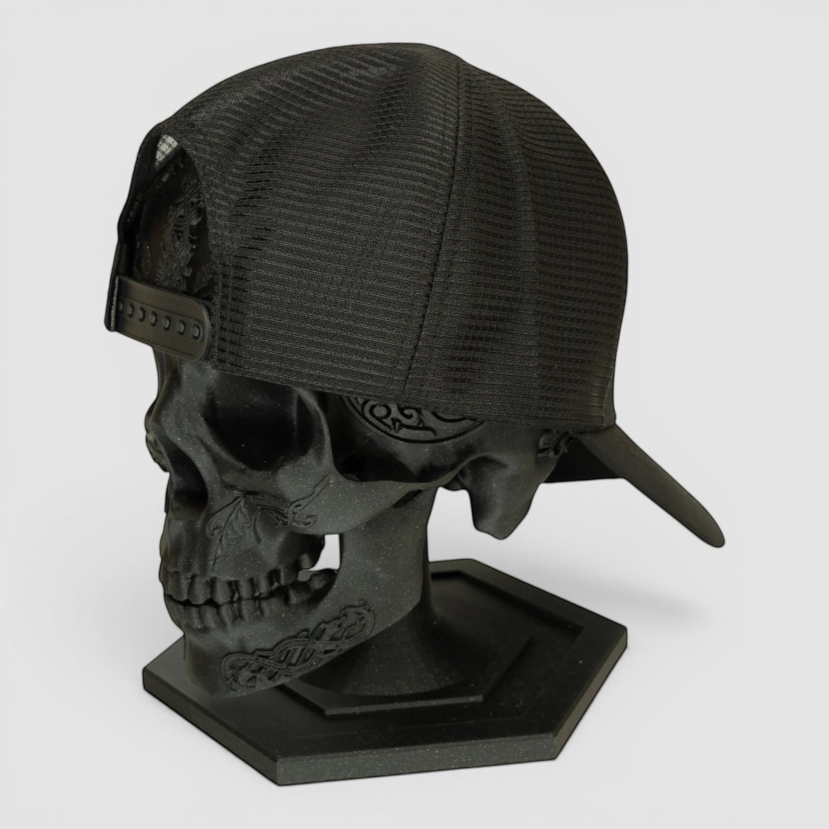 Night Heron Israel black mesh trucker cap displayed on a decorative black skull head stand